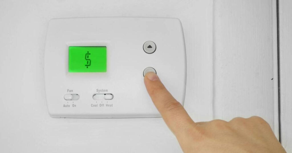 An individual's right pointer finger on the button of a thermostat, which displays the picture of a dollar sign.