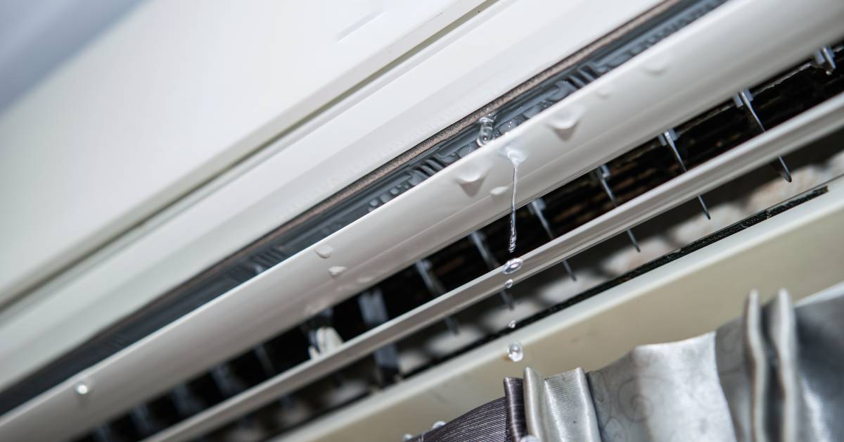 Close-up of an air conditioner leak. The unit sits on a wall, and water droplets hit the window curtains.