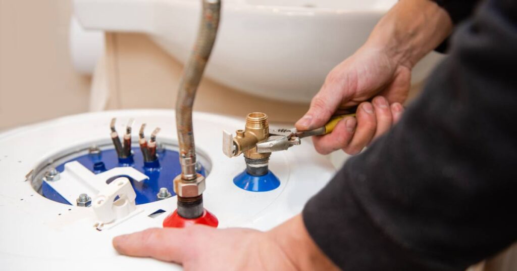 A close-up of someone adjusting a water heater component with a wrench. The person wears a black shirt.