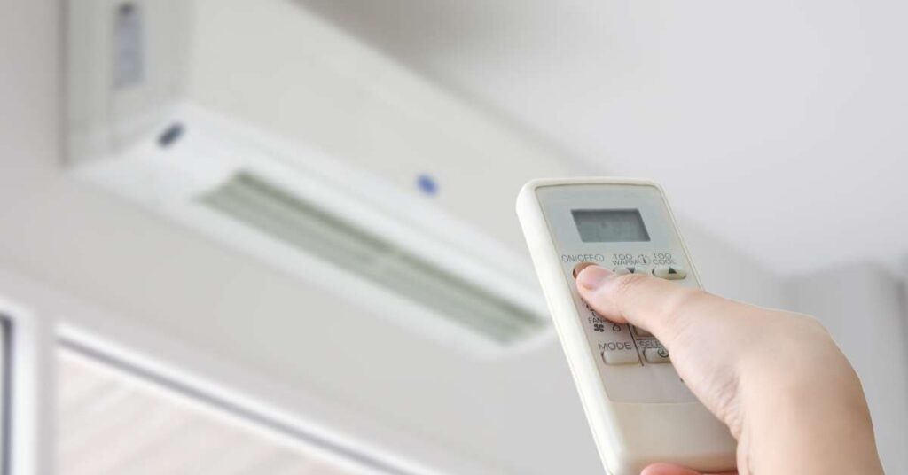 A close-up on a hand holding a remote control for a wall air conditioner unit that is mounted above a door or window.