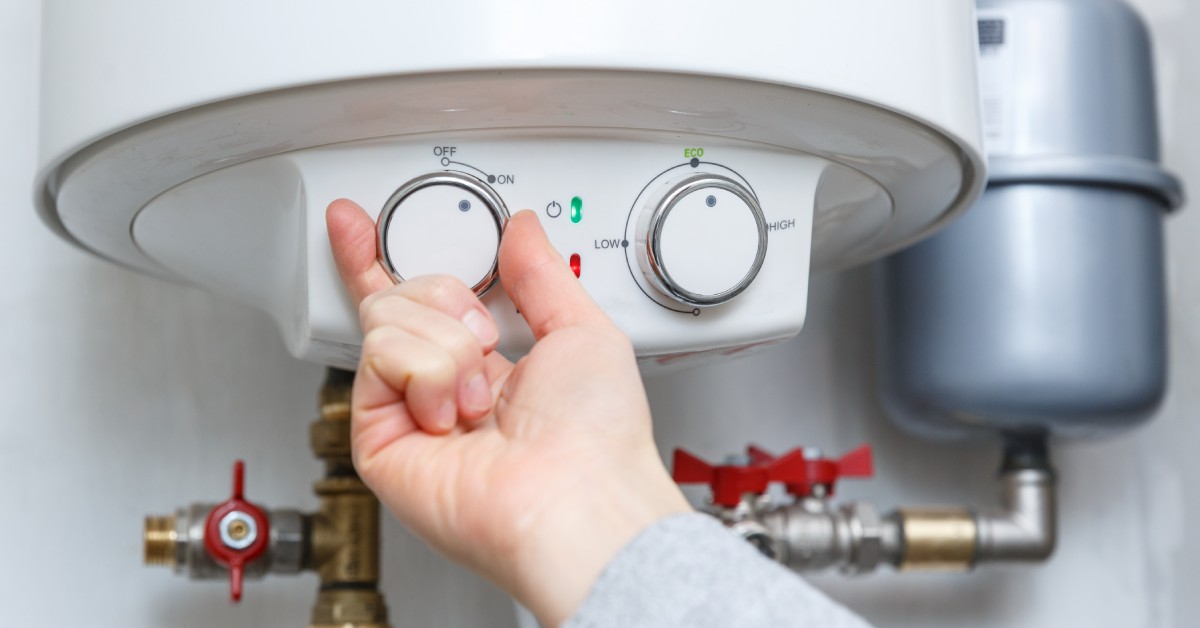 A close-up on a hand turning the temperature knob on an electric hot water heater, adjusting the settings.