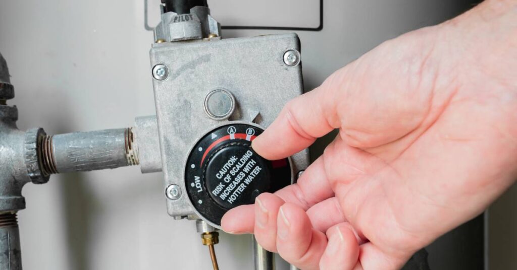 A focus on a hand holding the thermostat gauge of a hot water heater with a scalding warning on its face.