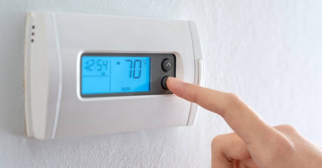 A hand extends a finger to adjust the temperature settings on a thermostat, which reads 70 degrees Fahrenheit.